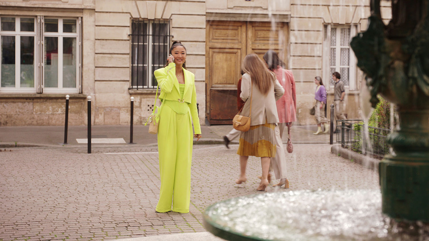 Mindy taking a phone call by the fountain at Place de l'Estrapade. (Photo: Tudum by Netflix)