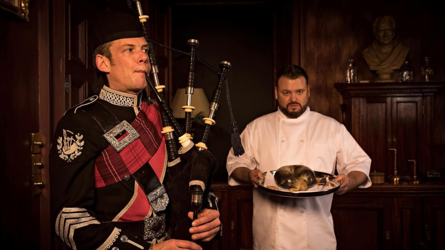 A bagpiper performing while the haggis is paraded into a room during Burns Night.